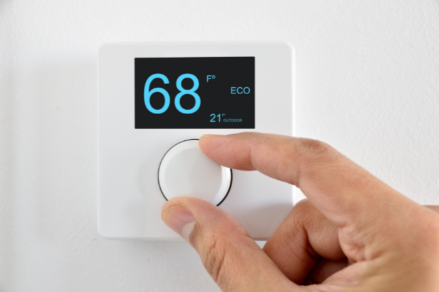 Closeup of a person’s hands adjusting the temperature on an electronic thermostat. 